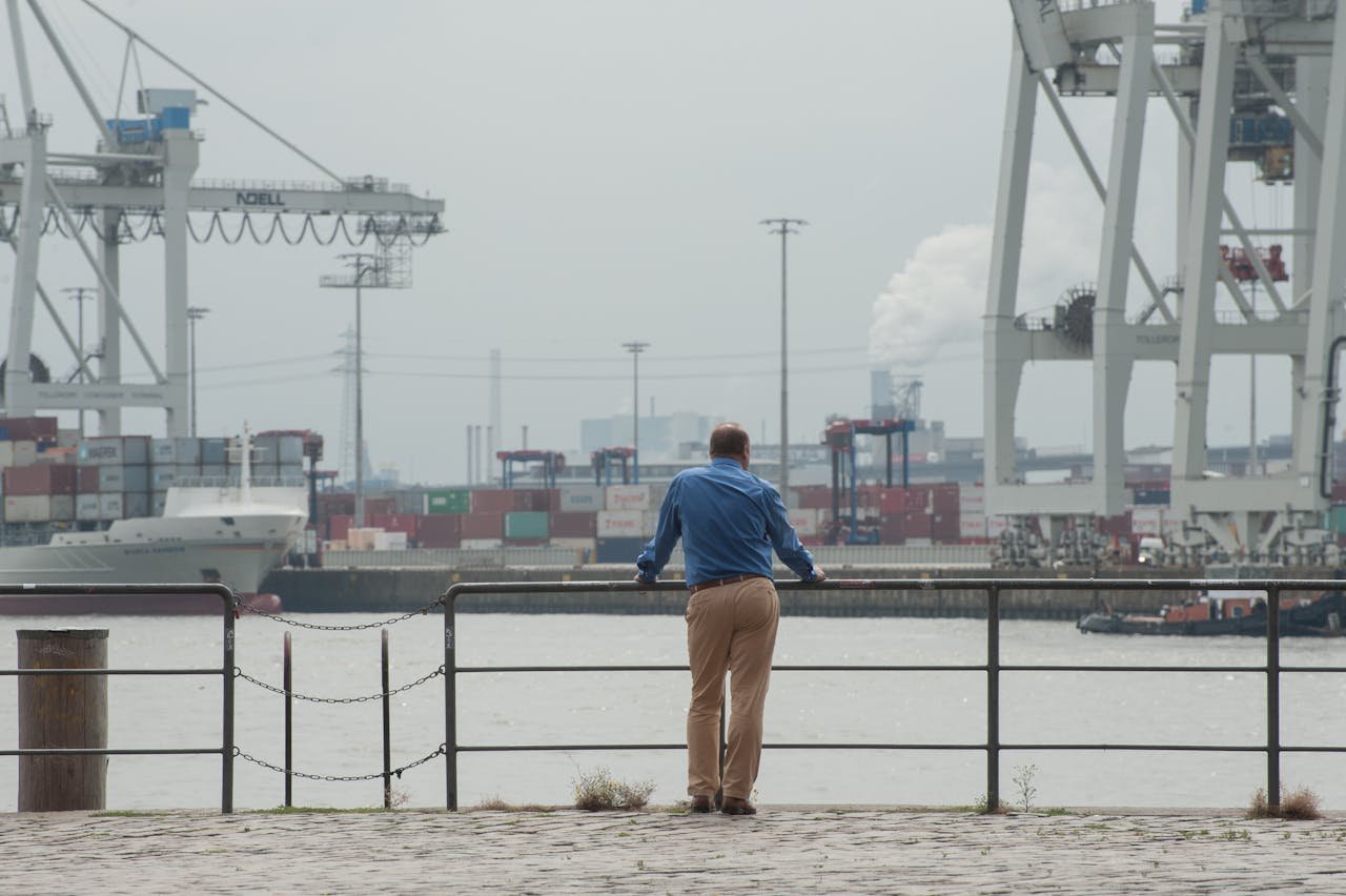 A man gazes at cargo ships in a foggy, industrial harbor scene.